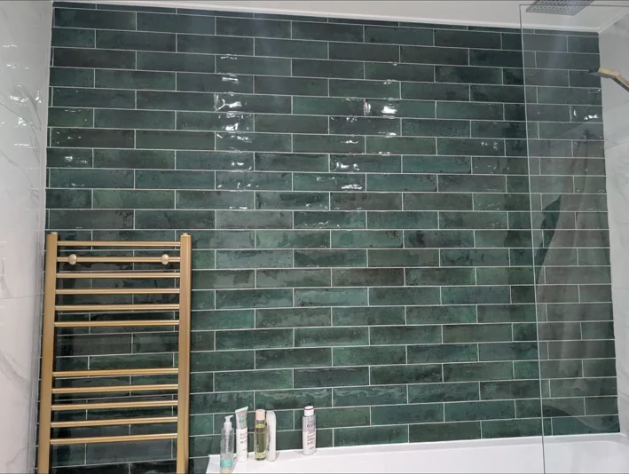 Green glazed wall tiles with gold heated towel rail