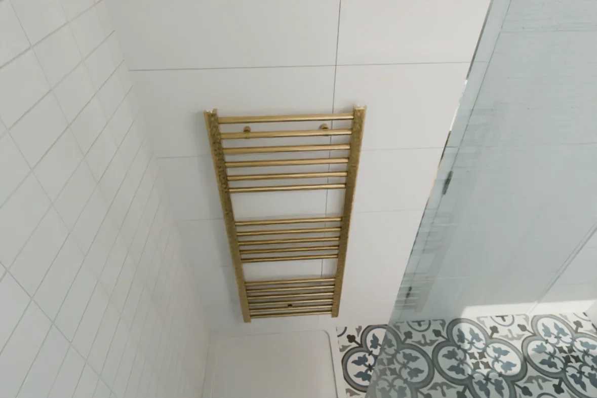 Gold heated towel rail beside patterned floor tiles
